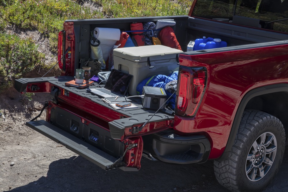 2026 GMC Sierra 1500 AT4X Crew Cab Short Box in Volcanic Red Tintcoat. Showing MultiPro Tailgate and MultiPro Audio System by Kicker; Camping props in bed